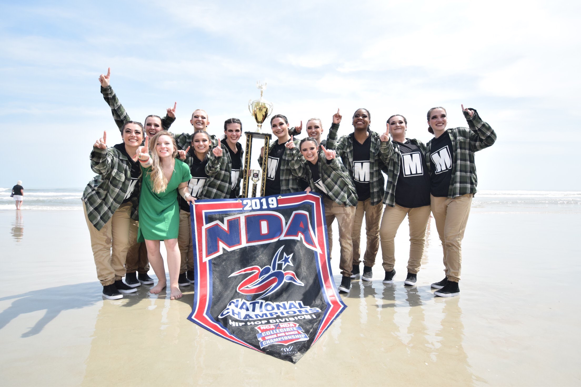 Jasper dancers posing with 2019 National Championship banner on beach